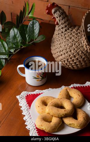 Vertikale Komposition einer rustikalen paraguayischen Frühstücksszene mit ringförmigen Chipas auf einem weißen Teller, serviert mit Cocido in einer Vintage-Blumenenam Stockfoto
