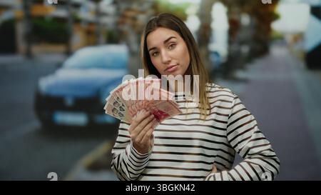 Frau, die isländische Krone draußen hält, mit einem nachdenklichen Ausdruck auf einem Stadtstraßenhintergrund. Stockfoto