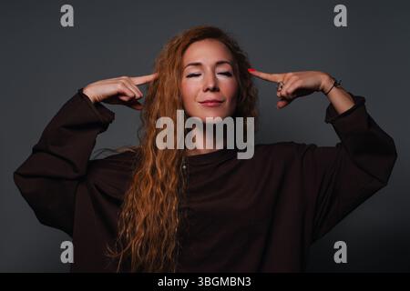 Junge schöne Frau berührt ihre Schläfe mit Fingern, Porträt auf grauem Hintergrund Stockfoto