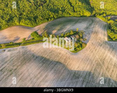 Aus der Vogelperspektive auf ein bewirtschaftetes Feld und ein verlassenes Bauernhaus in der ländlichen Landschaft des Cesane-Parks in der Nähe von Urbino, Marken, Mittelitalien Stockfoto
