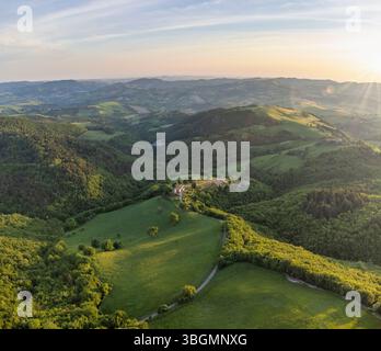 Blick aus der Vogelperspektive auf grüne Hügel, bewirtschaftete Felder und ein Bauernhaus in der ländlichen Landschaft des Cesane-Parks im Frühling, in der Nähe von Urbino, Marken, Zentralitalien Stockfoto