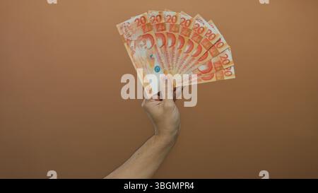 Hand eines kaukasiers, der mehrere philippinische Pesos vor braunem Hintergrund hält. Stockfoto