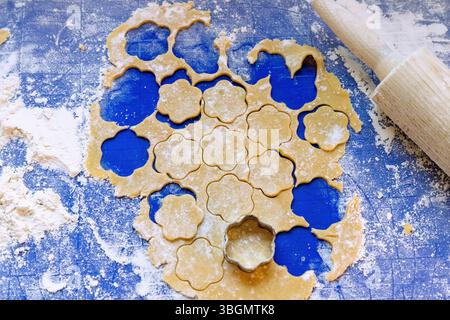 Ausgerollter Teig für Butterkekse mit Ausstecher und Kuchenrolle auf blauem Silikonboden Stockfoto