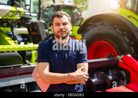 Porträt eines männlichen landwirtschaftlichen Fachmanns mit digitalem Tablet in der Nähe von Landmaschinen im Gerätehändler Stockfoto