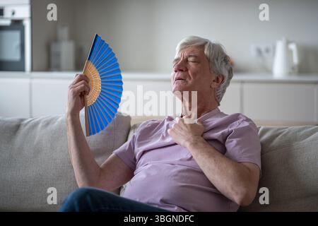 Ein älterer Mann fühlt sich schwindelig und unwohl durch Hitze und fächert sich zu Hause ohne Klimaanlage an. Hitzeleiden Stockfoto