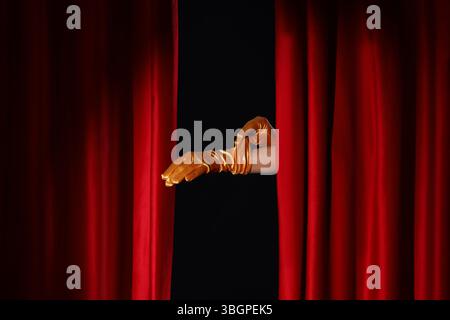 Weibliche Hände in Handschuhen hinter roten Vorhängen auf schwarzem Hintergrund Stockfoto