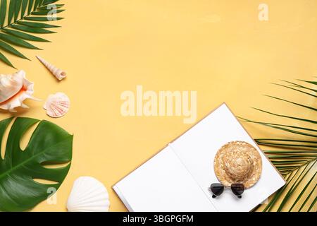 Komposition mit offenem Buch, kleinen Strandaccessoires, Muscheln und Palmblättern auf farbigem Hintergrund Stockfoto