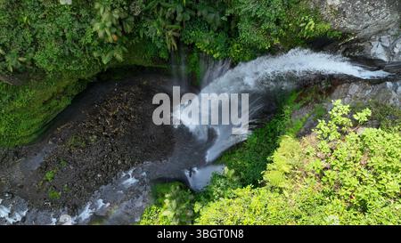 Der Tiu Kelep Wasserfall von oben zeigt seinen gewaltigen Abstieg in einen dunklen Pool, der von dichten tropischen Pflanzen in dieser atemberaubenden Luftszene eingerahmt wird. Stockfoto