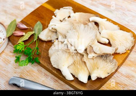 Es gibt einen Haufen roher Austernpilze auf dem Schneidebrett. Stockfoto