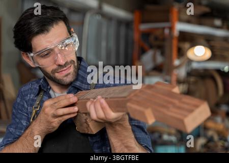 Porträt eines geschickten Zimmermanns, der in der Werkstatt einen hölzernen Gitarrenhals sorgfältig untersucht. Schutzbrille tragen und Handwerker präsentieren Stockfoto