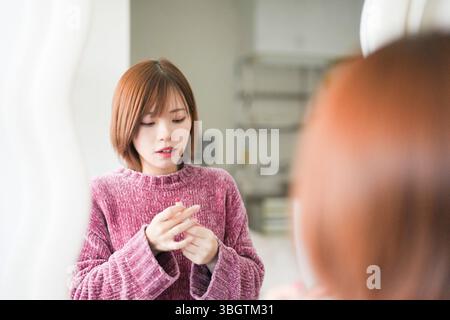In einem einfachen, sauberen Raum trägt eine junge schwangere Japanerin Anfang 20 mit kurzen braunen Haaren, ein rosa Strickkleid, Lippenstift in f Stockfoto