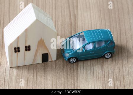 Charmantes Arrangement mit einem Miniatur-Holzhaus und einem Modellauto auf einer Holzoberfläche, perfekt für die Illustration von Haus- und Transportkonzepten Stockfoto
