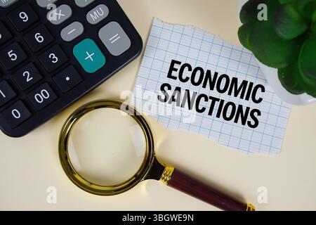 Text für wirtschaftliche Sanktionen mit Lupe und anc-Rechner auf gelbem Hintergrund Stockfoto