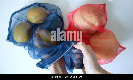 Foto von Obst und Gemüse in ökologischen Netztüten. Weißer Hintergrund. Drei Zitronen im blauen Beutel. Weibliche Hände, die Zitrone herausnehmen. Zwei Weißkohl Stockfoto