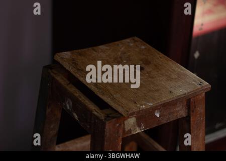 Stillleben eines alten, kaputten Holzhockers im Dunkeln, hervorgehoben durch dramatisches Licht. Ein Symbol des Vergessens, des Zeitverlaufs und der Nostalgie Stockfoto