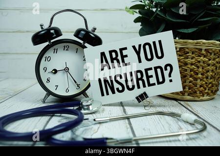 Sind Sie Versichert? Text auf Papierkarte mit Wecker und Stethoskop auf hölzernem Hintergrund Stockfoto