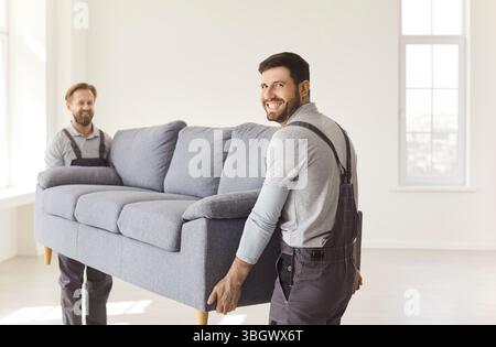 Zwei glückliche männliche Umzugswagen mit schwerem Sofa, transportieren Möbel während des Umzugstages Stockfoto