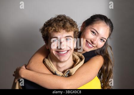 Nahaufnahme eines jungen erwachsenen Mannes, der seiner Freundin einen Huckepack gibt. Beide lächeln sorglos in die Kamera. Stockfoto