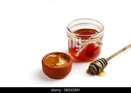 Ein Glas mit natürlichem Honig, umgeben von einem Löffel, ruht auf einem wunderschönen und charmanten Tontopf Stockfoto