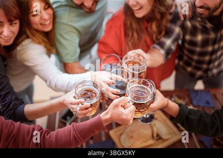 Blick aus einem Hochwinkel auf eine Gruppe von Freunden, die in einem Pub oder einer Party im Freien mit Bierbecher und Weingläsern lachen und rösten. Ein freudiger Moment der Feier Stockfoto