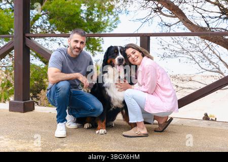 Ein lächelndes Paar mit Berner Sennenhund genießt im Frühling einen Moment im Freien Stockfoto