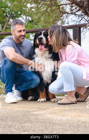 Ein lächelndes Paar mit Berner Sennenhund genießt im Frühling einen Moment im Freien Stockfoto