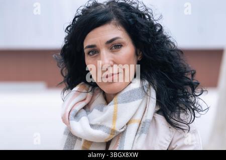 Horizontales Porträt einer Frau, die auf einer Bank sitzt und Wintermantel und Schal trägt Stockfoto