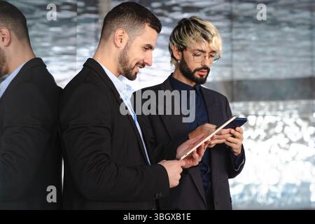 Zwei Geschäftsleute in Anzügen, die in modernen Glasbüros mit digitalen Tablets arbeiten Stockfoto