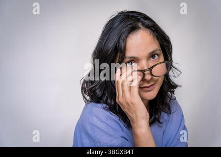 Nahaufnahme einer jungen erwachsenen hispanischen Frau in ihren 40ern mit Brille im Studio mit lässiger Kleidung. Konzept der Augenpflege und Sehpflege und Brille Stockfoto