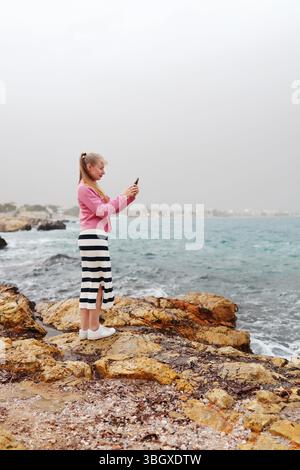 Coastal Tourism Concept Frau in lässigem Outfit, die ein Foto an einem windigen Ufer macht. Stockfoto