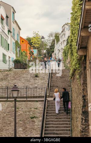 Ein Paar, von hinten gesehen, geht Hand in Hand eine malerische Steintreppe im historischen Viertel Montmartre von Paris hinauf, umgeben von charmantem B Stockfoto
