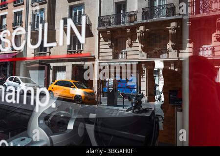 Eine dynamische Pariser Straßenszene, die durch ein Schaufenster aufgenommen wurde und die Reflexionen eines orangen Autos und klassischer Gebäude mit Text oder Gegenständen überlagert Stockfoto