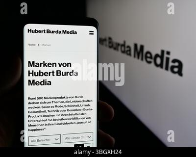 Stuttgart, Deutschland - 03.07.2025: Person, die ein Handy hält, mit Webseite der deutschen Hubert Burda Media Holding KG auf dem Bildschirm vor dem Logo. Stockfoto