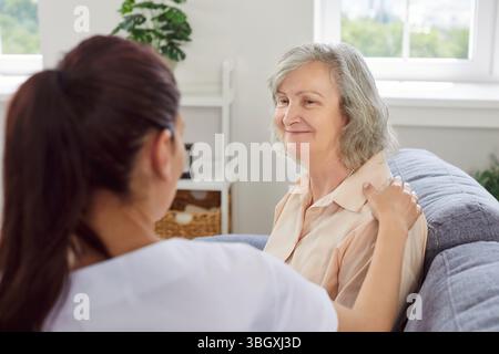 Eine ältere Frau sitzt auf dem Sofa mit einer jungen freundlichen Krankenschwester, die sie zu Hause besucht Stockfoto