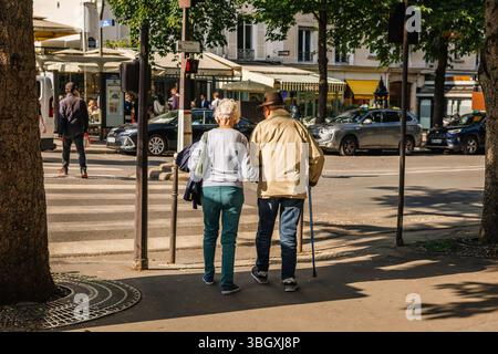 Ein herzerwärmender Blick von hinten auf ein älteres Paar, das zusammen auf einem sonnigen Bürgersteig der Stadt spaziert, der Mann mit einem Stock, der eine lebenslange Koma verkörpert Stockfoto