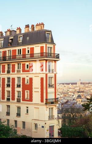 Ein wunderschönes und unverwechselbares Apartmentgebäude mit rot-weiß gemusterter Fassade steht hoch im Viertel Montmartre, mit dem Pariser Stadtbild Stockfoto
