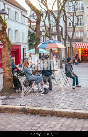 Am belebten Place du Tertre in Montmartre konzentriert sich ein talentierter Straßenkünstler darauf, ein Frauenporträt zu malen und die lebendige Kunst einzufangen Stockfoto