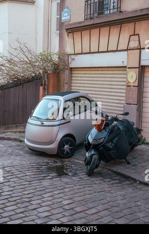 Ein futuristisches, silbernes Elektroauto parkt neben einem Roller in einer klassischen Kopfsteinpflasterstraße in Paris und bietet eine moderne Lösung für urbane Motive Stockfoto