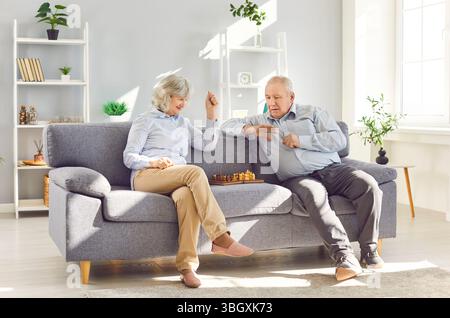 Älteres altes Paar, das gemeinsam Schach spielt und zu Hause auf dem Sofa sitzt. Stockfoto