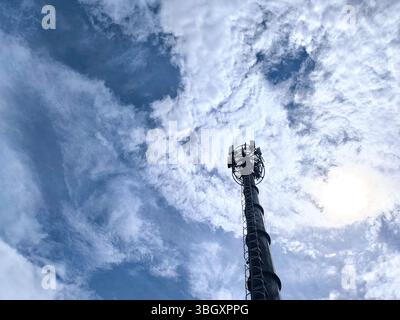 Der Telekommunikationsturm steht hoch mit einem Hintergrund aus hellen weißen Wolken und einem blauen Himmel Stockfoto