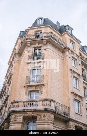 Ein flacher Eckblick auf ein elegantes Pariser Apartmenthaus mit kunstvoll verzierten schmiedeeisernen Balkonen, detaillierten Steinschnitzereien an der Basis und en Stockfoto