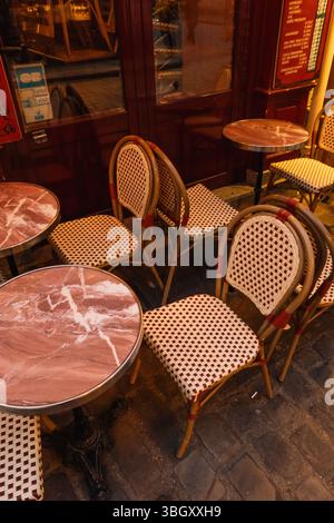 Die klassischen Korbstühle und die Tische mit Marmorplatte einer leeren Pariser Caféterrasse warten nachts auf Gäste auf einem Bürgersteig und schaffen so ein charmantes an Stockfoto