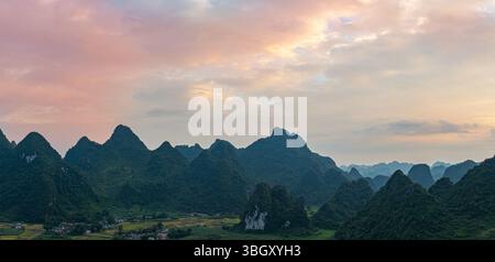 Ein atemberaubender Blick aus der Luft auf einen dramatischen Sonnenaufgang, der den Himmel mit leuchtenden Orange- und Rottönen über nebelbedeckten Karstbergen beleuchtet. Die Ruhe l Stockfoto