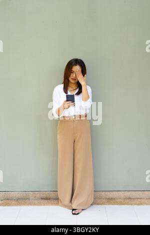 Porträt einer Frau in voller Länge, die Geschäftskleidung mit Telefon gegen eine normale Wand trägt Stockfoto