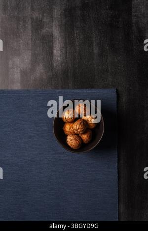 Schwarze Schüssel mit Walnüssen und blauem Tischtuch auf schwarzem Tafel Hintergrund. Flache Lagen. Draufsicht. Stockfoto
