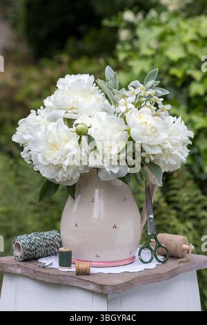 Strauß aus weißen Pfingstrosenblüten in einer rustikalen Vase im Garten Stockfoto