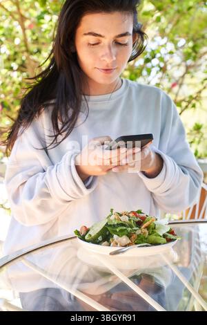 Eine Frau, die beim Mittagessen etwas auf ihrem Handy nachsieht Stockfoto