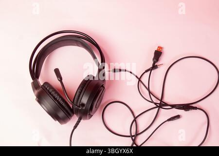 Schwarzes Gaming-Headset mit Mikrofon und Kabeln auf rosafarbener Oberfläche Stockfoto