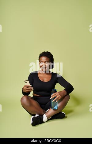 Eine junge, fitte afroamerikanische Frau macht während ihres Workouts eine Pause, schlürft Wasser und lächelt. Stockfoto