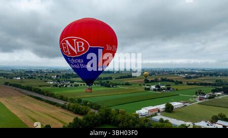 Bird in Hand, Pennsylvania, 13. September 2024 - farbenfrohe Heißluftballons schweben anmutig über die üppigen grünen Felder von Pennsylvania. Der bewölkte Himmel sorgt für eine ruhige Atmosphäre, während die Menschen die einzigartige Aussicht von oben genießen. Stockfoto